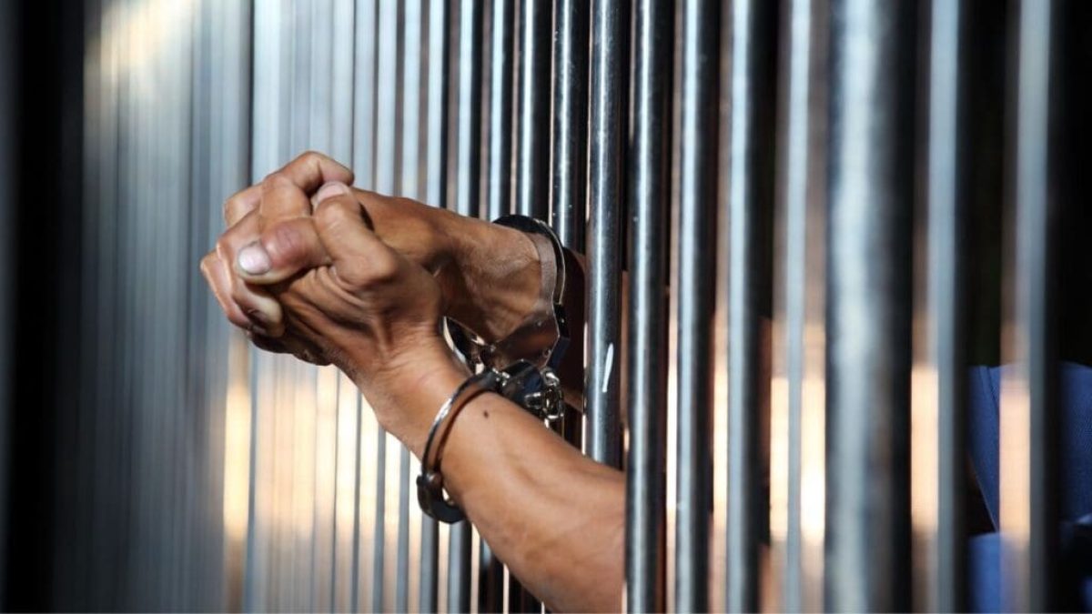 Hands in Handcuffs Gripping Jail Bars